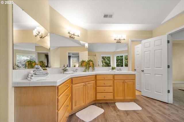 full bath with visible vents, a sink, wood finished floors, double vanity, and lofted ceiling