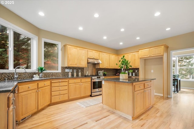 kitchen featuring stainless steel gas range oven, backsplash, light brown cabinets, and under cabinet range hood