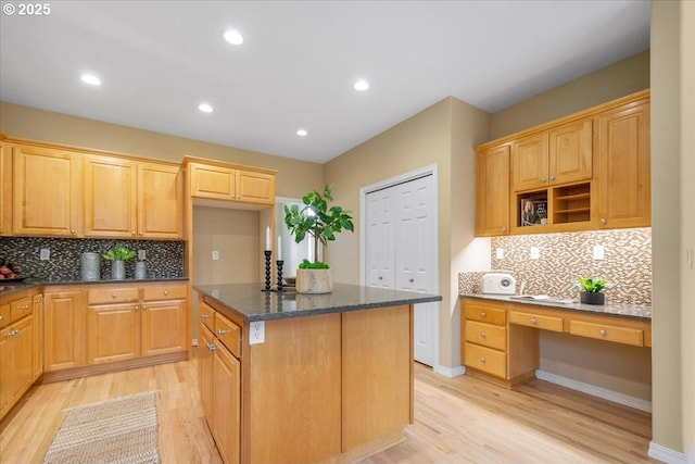 kitchen with built in desk, a center island, light wood-type flooring, and dark stone counters