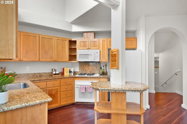 kitchen featuring dark wood-type flooring, tasteful backsplash, light brown cabinets, white appliances, and light stone countertops