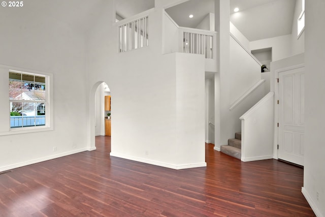 unfurnished living room with dark wood-type flooring and a towering ceiling