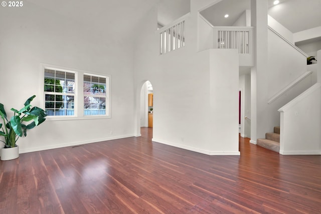 unfurnished living room featuring dark wood-type flooring and a towering ceiling