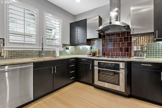 kitchen featuring sink, ventilation hood, light wood-type flooring, stainless steel appliances, and decorative backsplash