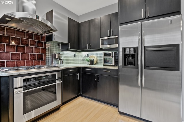 kitchen with tasteful backsplash, light stone counters, ventilation hood, appliances with stainless steel finishes, and light hardwood / wood-style floors