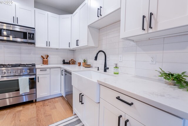 5253 NE 32nd Pl, Portland, OR 97211 - kitchen with appliances with stainless steel finishes, a sink, white cabinetry, light wood-style flooring, and backsplash