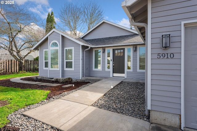 property entrance with fence and roof with shingles