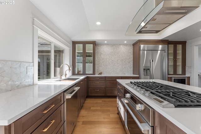 kitchen featuring glass insert cabinets, wall chimney exhaust hood, appliances with stainless steel finishes, and a sink