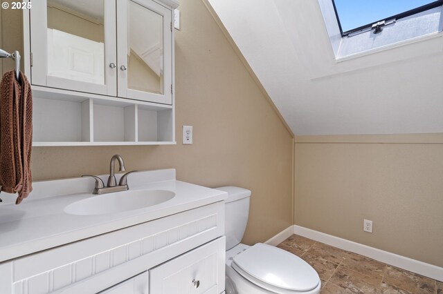 bathroom featuring a skylight, toilet, vanity, and baseboards