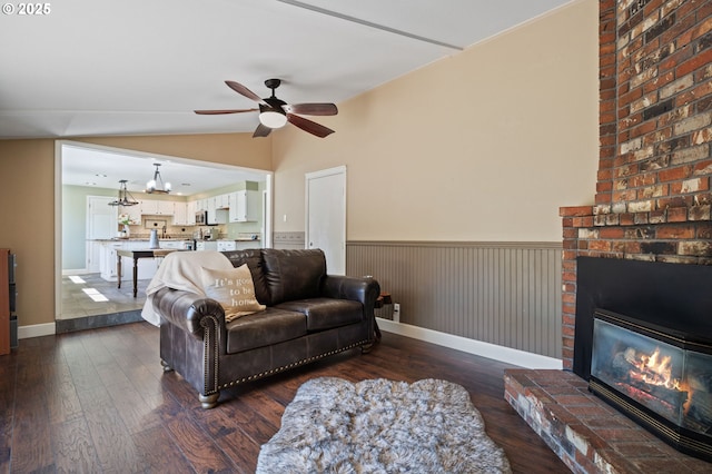 living area with ceiling fan, dark wood-style floors, lofted ceiling, a fireplace, and wainscoting