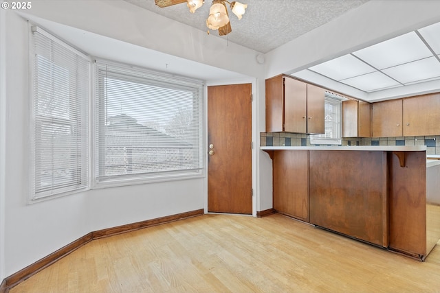 kitchen with a breakfast bar, light hardwood / wood-style flooring, a textured ceiling, kitchen peninsula, and ceiling fan