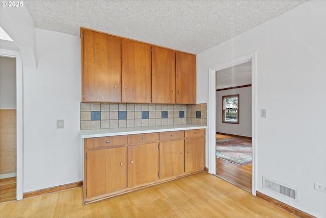 kitchen with a textured ceiling, light hardwood / wood-style flooring, and backsplash