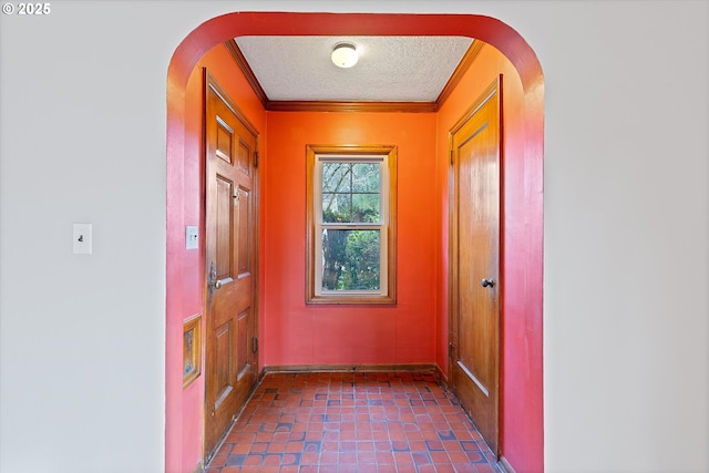 doorway featuring dark tile patterned floors, ornamental molding, and a textured ceiling