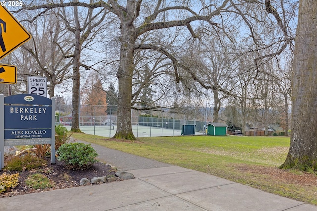 view of property's community with a storage shed, tennis court, and a lawn