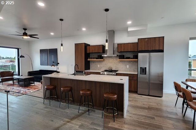280 NW Huckleberry St, Waldport, OR 97394 - kitchen featuring stainless steel fridge, wall chimney range hood, a sink, light wood-style flooring, and light countertops