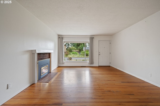 10438 NE Davis St, Portland, OR 97220 - unfurnished living room featuring wood finished floors, a tiled fireplace, a textured ceiling, and baseboards