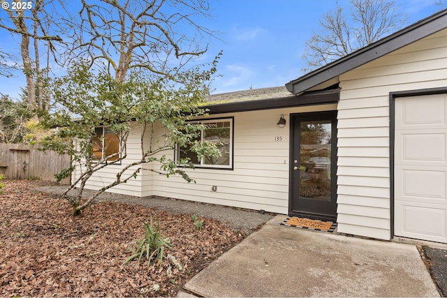 view of exterior entry with a garage and fence