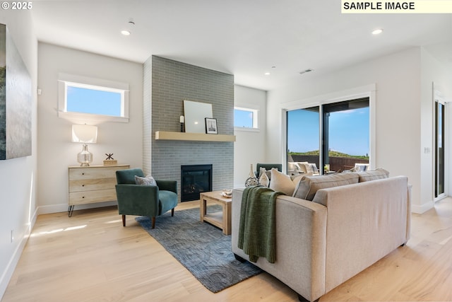 living room with a brick fireplace, a healthy amount of sunlight, and light hardwood / wood-style floors