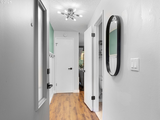 corridor featuring hardwood / wood-style flooring, a notable chandelier, and a textured ceiling