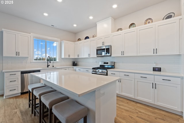 16679 SW Darwin Loop, Portland, OR 97224 - kitchen featuring appliances with stainless steel finishes, a kitchen bar, a sink, light wood-style floors, and white cabinetry