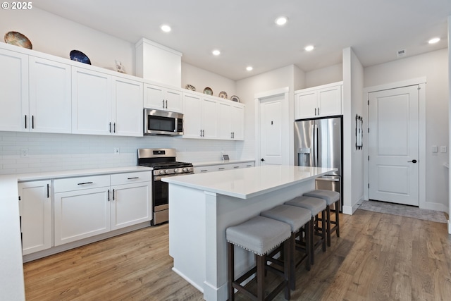 16679 SW Darwin Loop, Portland, OR 97224 - kitchen with stainless steel appliances, a breakfast bar, light wood finished floors, decorative backsplash, and white cabinetry