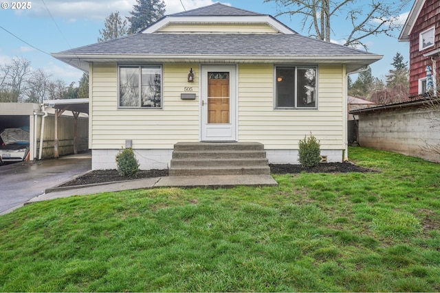 bungalow-style home featuring entry steps, an attached carport, roof with shingles, fence, and a front yard