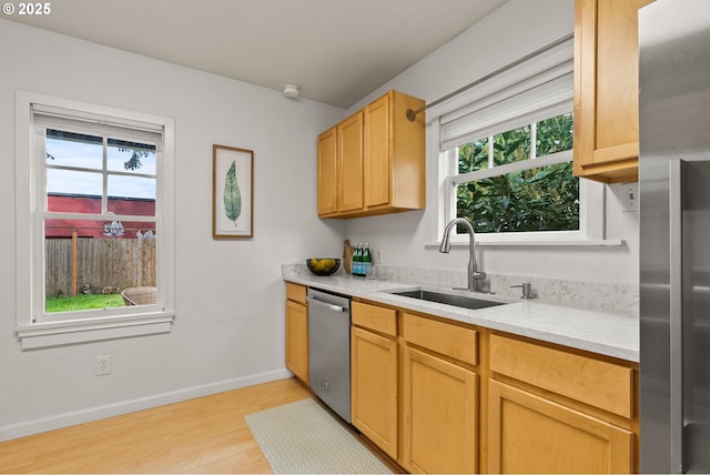 kitchen with stainless steel appliances, light wood-style flooring, a sink, baseboards, and light stone countertops