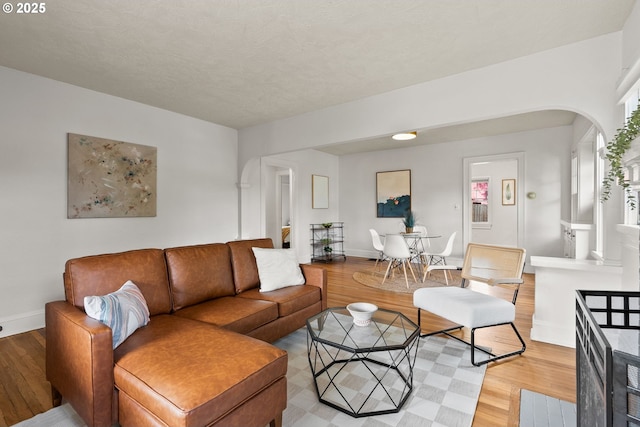 living room with arched walkways, light wood-type flooring, and baseboards