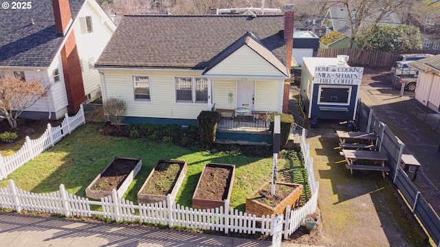 exterior space featuring fence private yard, a garden, roof with shingles, a chimney, and a front yard