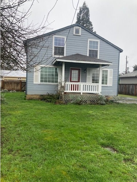 rear view of house with covered porch, a lawn, and fence