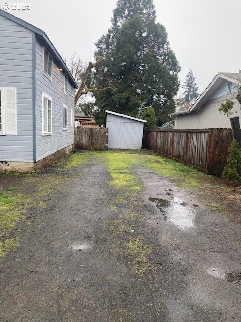 view of yard with an outdoor structure, a storage unit, fence, and driveway