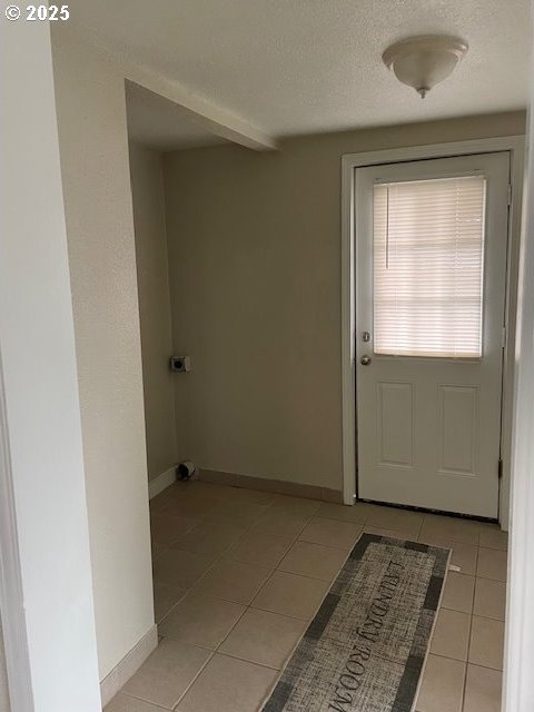 doorway to outside featuring light tile patterned floors, baseboards, and a textured ceiling