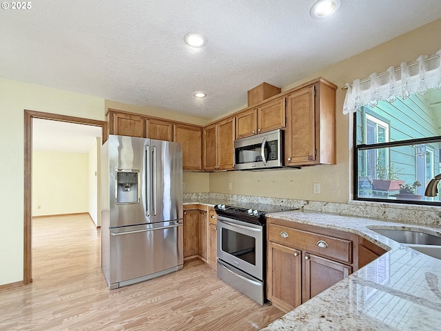 550 Velopa Ct, Brookings, OR 97415 - kitchen featuring stainless steel appliances, a sink, light wood-type flooring, light stone counters, and a textured ceiling