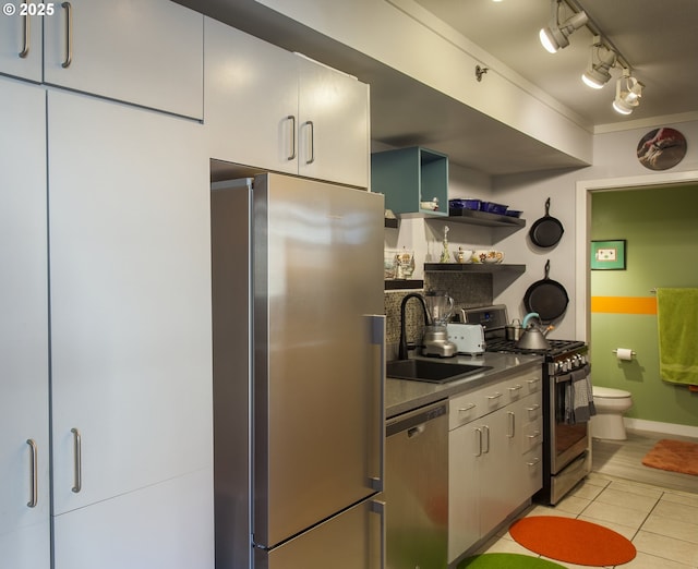 533 NE Holladay St Unit 308, Portland, OR 97232 - kitchen with appliances with stainless steel finishes, dark countertops, light tile patterned flooring, open shelves, and track lighting