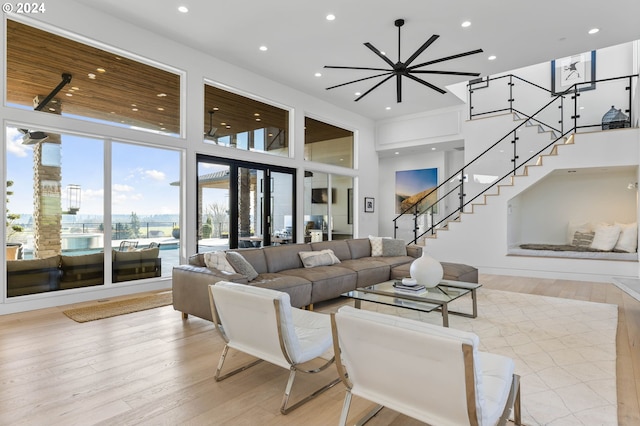 living room with a towering ceiling, recessed lighting, light wood-style flooring, and stairs