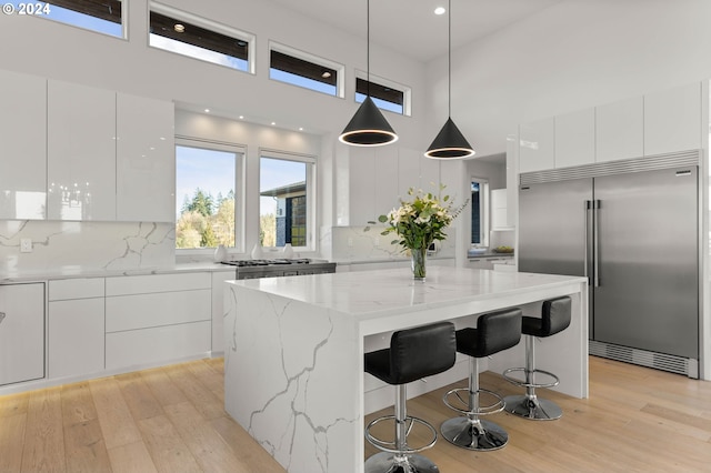 kitchen with light wood-type flooring, modern cabinets, a kitchen island, built in fridge, and white cabinets