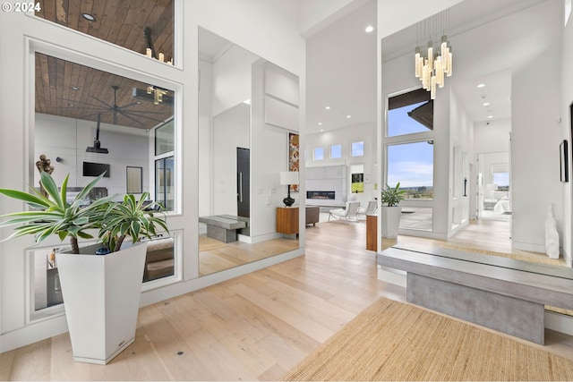 foyer entrance with a glass covered fireplace, a notable chandelier, wood finished floors, and a towering ceiling