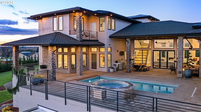 rear view of house featuring stucco siding, a pool with connected hot tub, stone siding, a patio, and a balcony