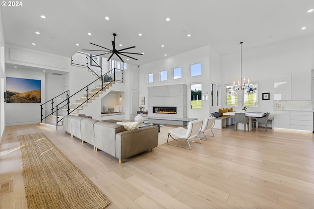 living room featuring light wood-type flooring, an inviting chandelier, a towering ceiling, stairs, and a tile fireplace