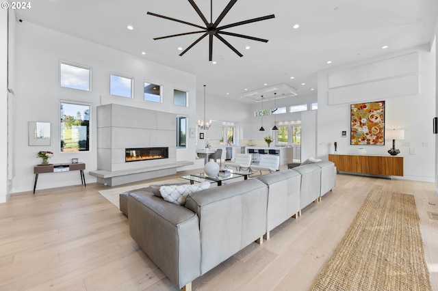 living area with a glass covered fireplace, a towering ceiling, recessed lighting, light wood finished floors, and a chandelier