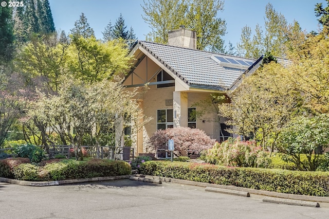 6645 W Burnside St Unit 515, Portland, OR 97210 - view of front of house featuring a chimney, a tile roof, stucco siding, solar panels, and uncovered parking
