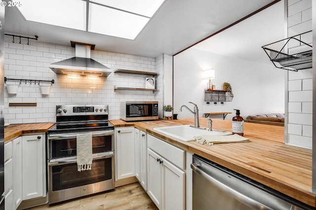 kitchen with stainless steel appliances, a sink, wall chimney exhaust hood, decorative backsplash, and butcher block countertops