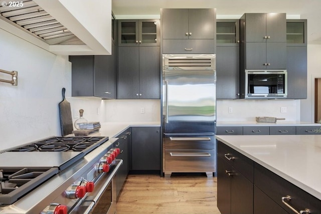 kitchen with custom exhaust hood, light hardwood / wood-style flooring, and built in appliances