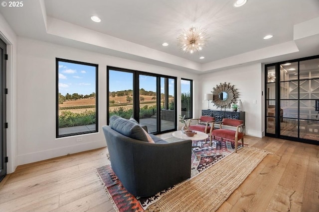 living room with a tray ceiling, a chandelier, and light wood-type flooring