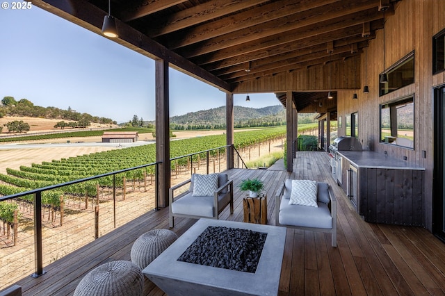 wooden deck with a fire pit, a mountain view, a rural view, and an outdoor kitchen