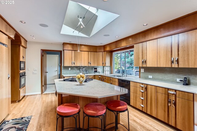 7145 SW Gable Pkwy, Portland, OR 97225 - kitchen featuring a skylight, black appliances, light wood finished floors, tasteful backsplash, and recessed lighting