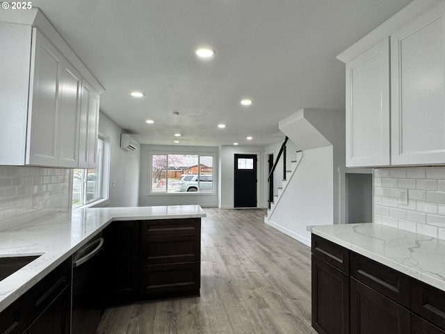 kitchen featuring black dishwasher, light wood-style flooring, light stone counters, an AC wall unit, and white cabinetry