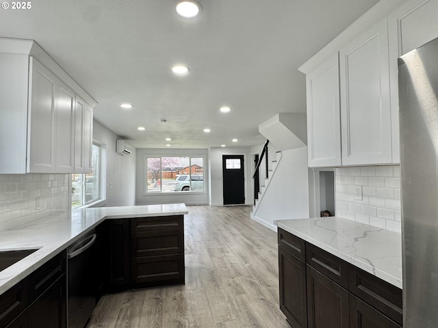 kitchen featuring a wall unit AC, black dishwasher, stainless steel refrigerator, light stone countertops, and light wood finished floors