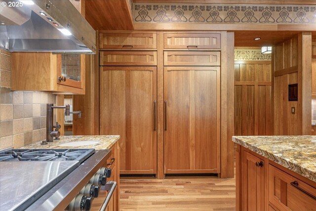 13150 SW Iron Mountain Blvd, Portland, OR 97219 - kitchen featuring range hood, brown cabinets, light wood-style floors, light stone counters, and decorative backsplash