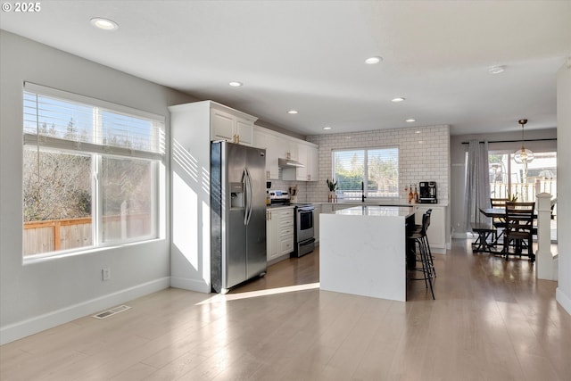 kitchen with light wood finished floors, appliances with stainless steel finishes, backsplash, and under cabinet range hood