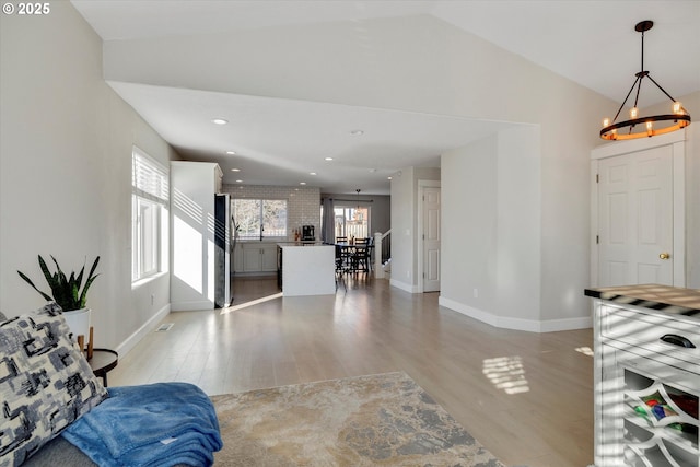 living room with baseboards, lofted ceiling, light wood-type flooring, a notable chandelier, and recessed lighting